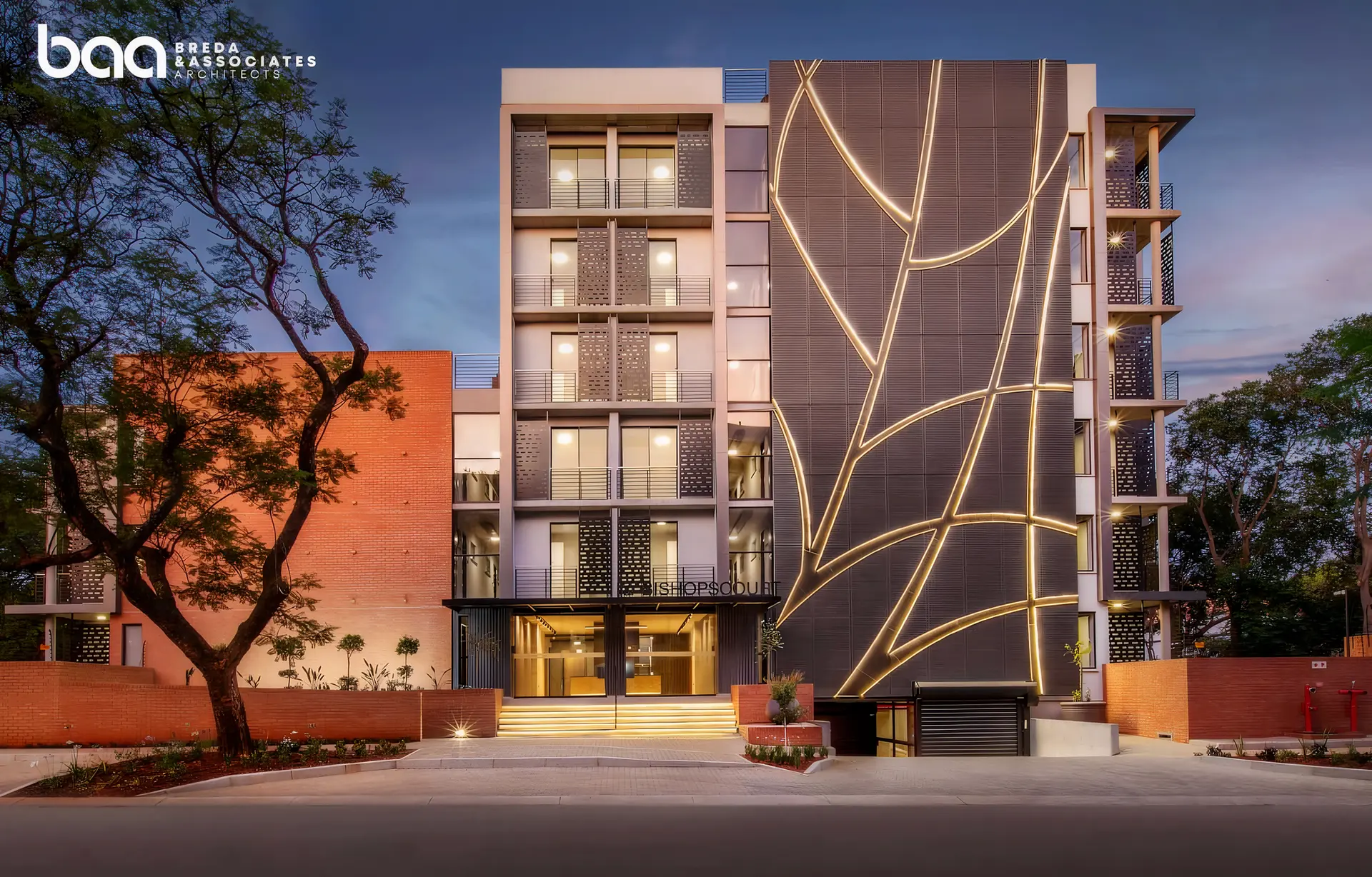 Night view of the iQ Bishopscourt apartment building in Brooklyn, Pretoria, developed by Uniqon. The facade features a distinctive illuminated tree-branch geometric design and a modern glass entrance.