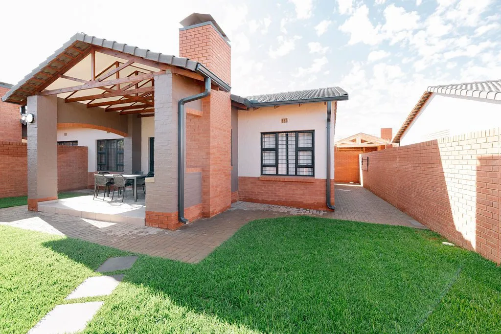 Spacious garden and covered entertainment patio at a simplex unit in iQ Rheenendal Ext 85, Rietvalleirand. The home features low-maintenance face brick, a built-in braai, and modern architectural detailing.