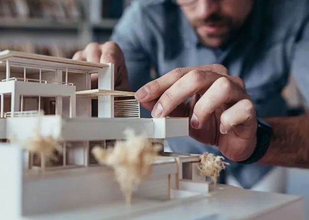Close-up of an architect carefully adjusting a scale model for a new residential project, symbolizing Uniqon's commitment to meticulous planning and expert partnerships.